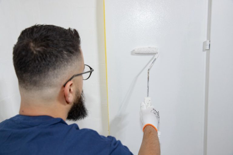 Ein Mann streicht eine Wand weiß mit einem Farbroller